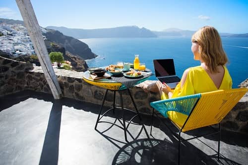 woman using a laptop and eating breakfast in front of a scenic view on vacation