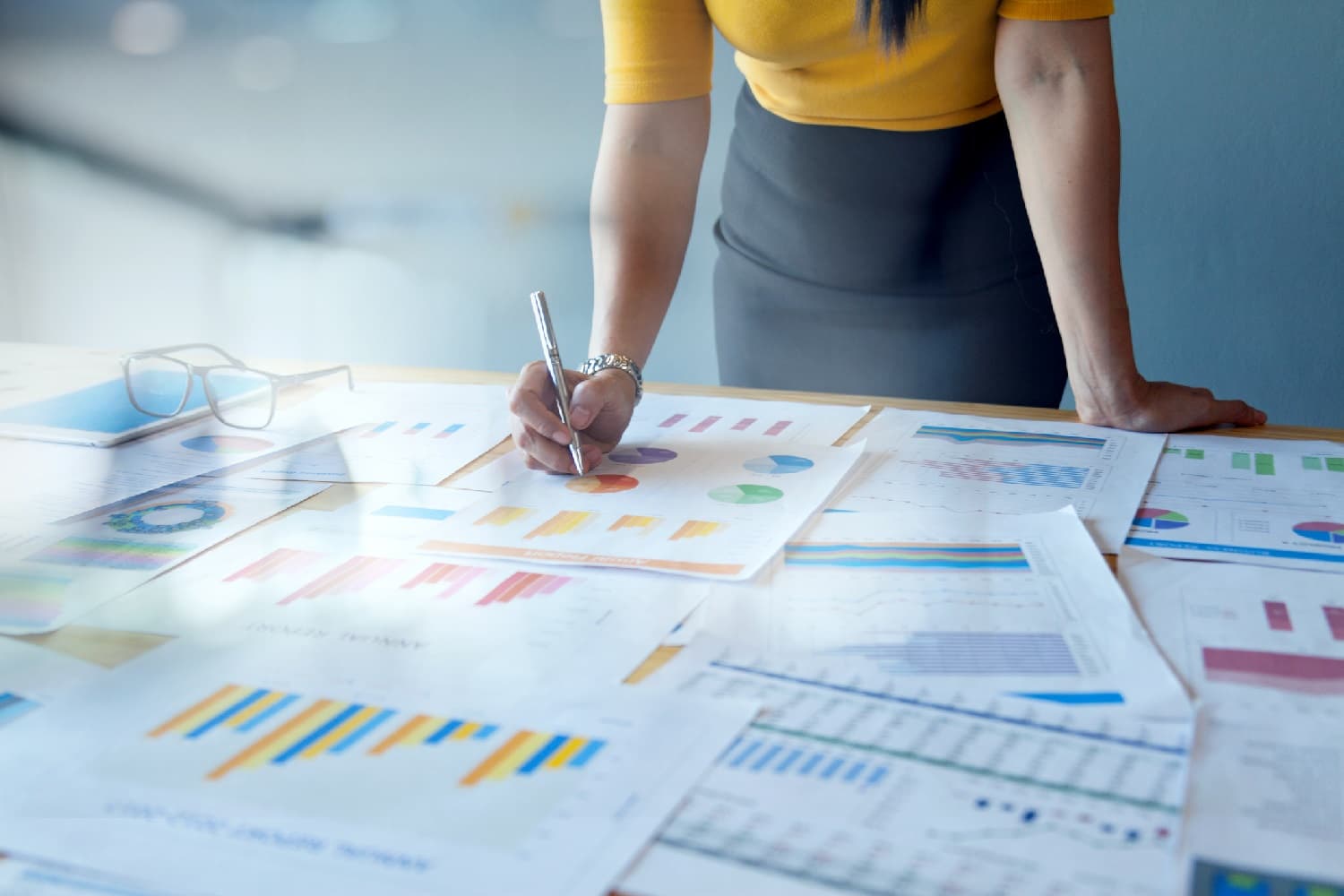 businesswoman standing over a series of paper reports on a desk