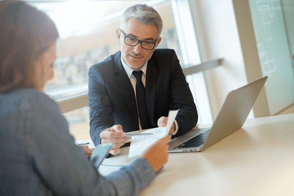 businessman looking over someone's papers at a desk