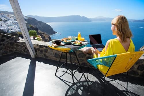 woman using a laptop and eating breakfast in front of a scenic view on vacation
